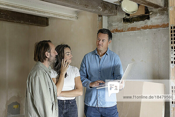 Mature couple with contractor discussing over laptop at construction site