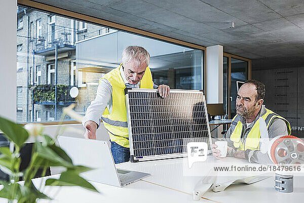 Engineer with solar panel explaining colleague over tablet PC at office