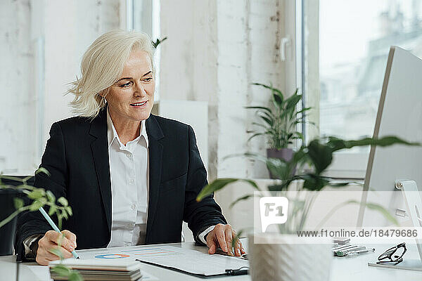 Smiling businesswoman working with documents on desk in office