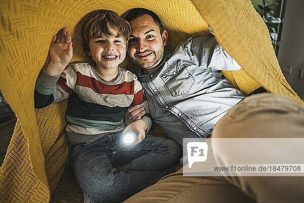 Glücklicher Vater und Sohn mit Fackel unter gelber Decke