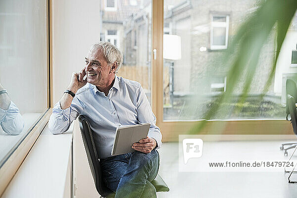 Happy businessman with tablet PC sitting on chair at workplace
