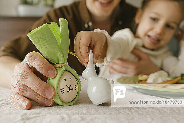 Father and daughter holding bunny and Easter egg at table at home