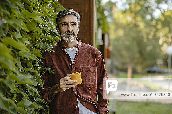 Mature man holding coffee cup at overgrown facade