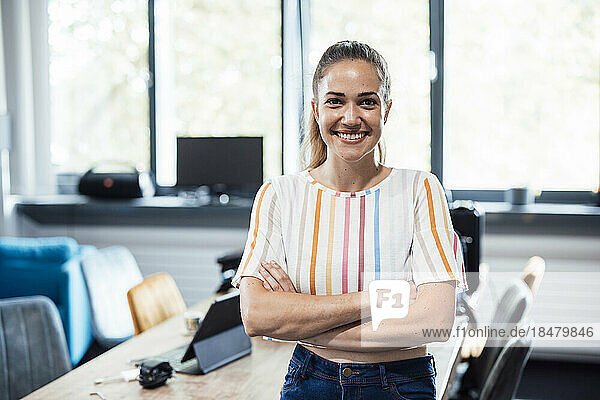 Happy businesswoman standing with arms crossed in office