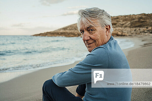 Smiling senior man with gray hair sitting at beach