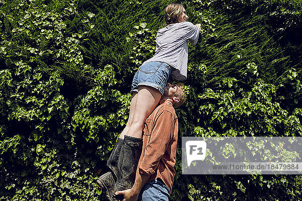 Boyfriend lifting girlfriend near plants on sunny day