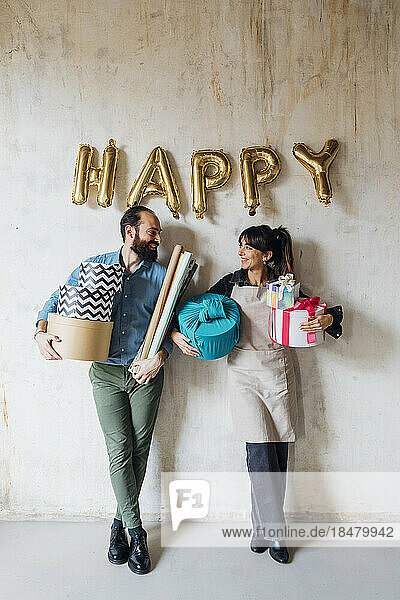 Glückliches Paar hält Geschenkboxen in der Hand und lehnt an der Wand
