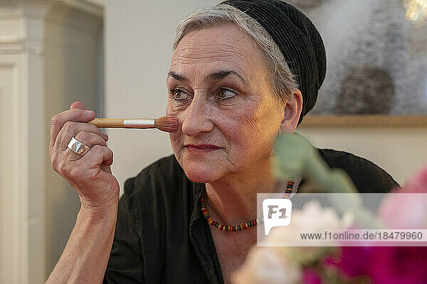 Senior woman applying make-up with brush at home