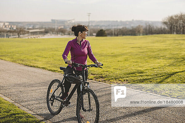 Mature woman standing with bicycle on sunny day