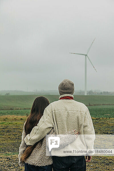 Teenage couple standing together looking at wind turbine
