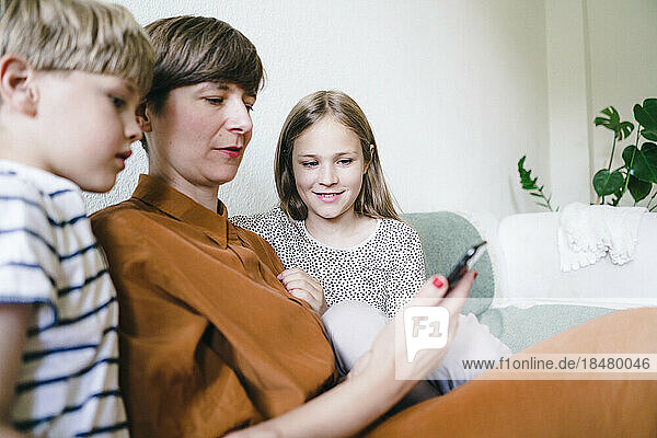 Woman watching smart phone with son and daughter sitting at home