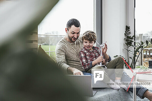 Father watching laptop with son sitting at home
