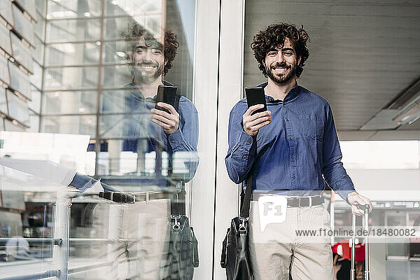 Happy businessman standing with smart phone at railroad station