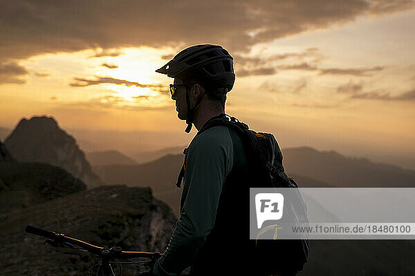Mountainbiker unter bewölktem Himmel bei Sonnenuntergang