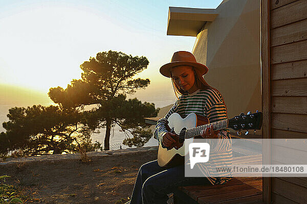 Young woman playing guitar at sunset