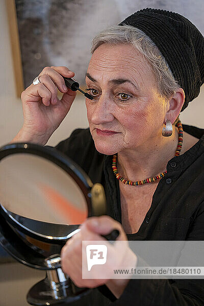 Woman in skullcap applying mascara at home