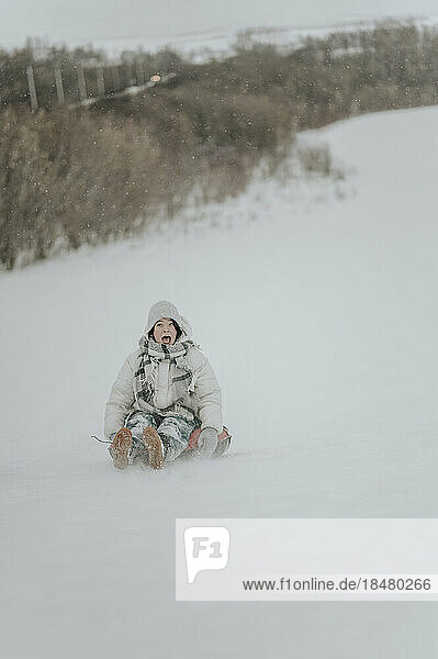 Fröhliches Teenager-Mädchen reitet aufblasbaren Schlitten im Schnee