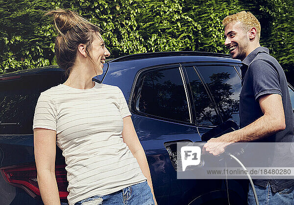 Happy woman talking to boyfriend charging electric car