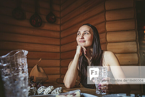 Smiling woman with drinking glass contemplating in sauna