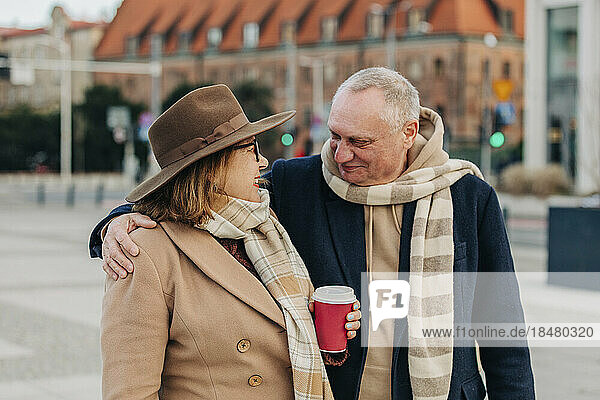 Smiling senior man embracing woman holding disposable cup