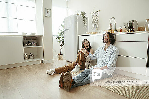 Happy couple sitting on floor in kitchen at home