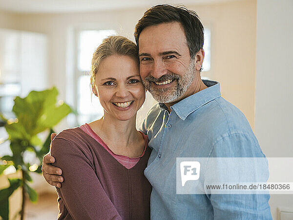 Happy mature man with arm around wife at home