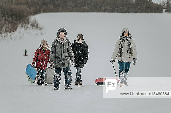 Happy family walking with inflatable sled in snow
