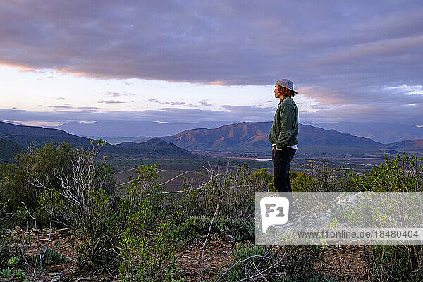 Junger Mann steht bei Sonnenuntergang auf einem Felsen