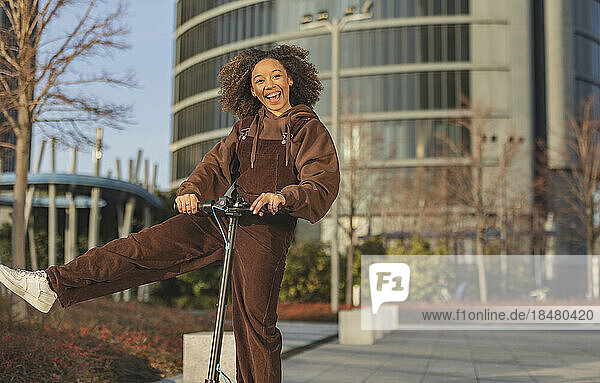 Cheerful woman having fun and riding push scooter on footpath