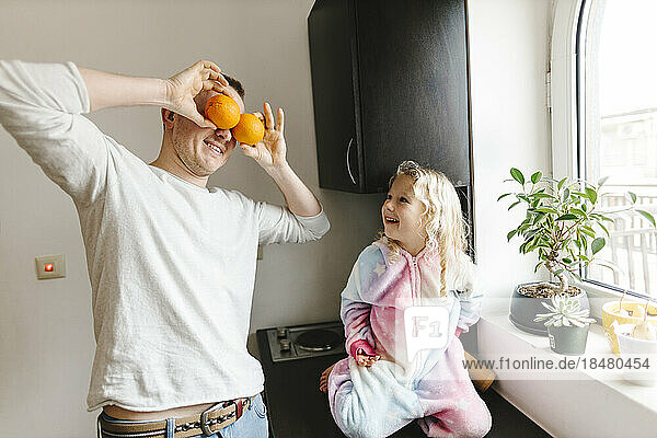Glückliche Tochter schaut den Vater an  der Orangen über die Augen hält