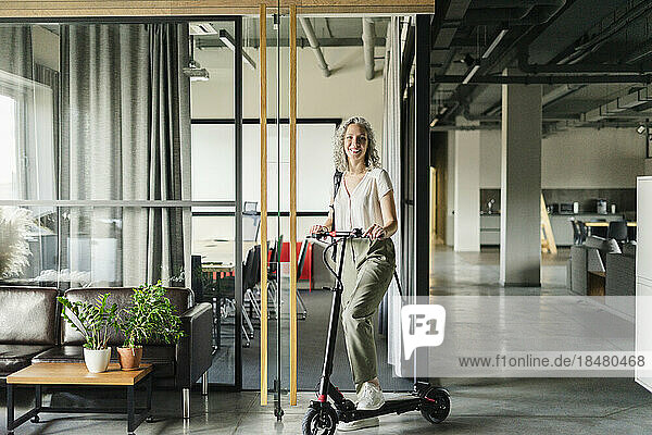 Portrait of smiling businesswoman with electric scooter in office