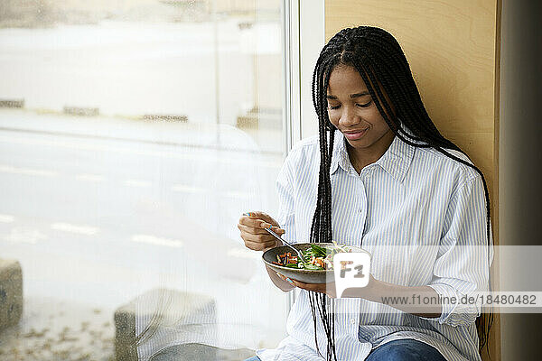 Smiling woman eating salad near window