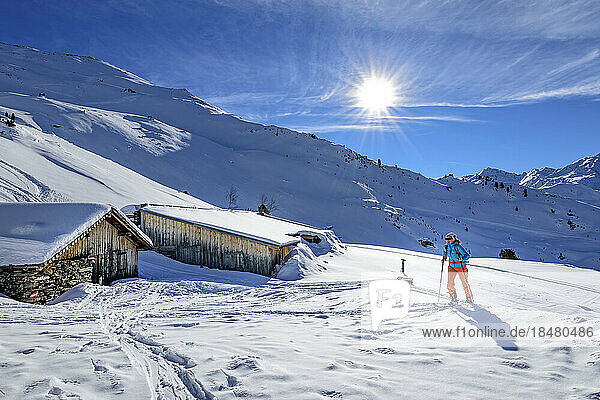 Österreich  Tirol  Sonne scheint über einer Skifahrerin  die an einsamen Hütten in den Tuxer Alpen vorbeifährt