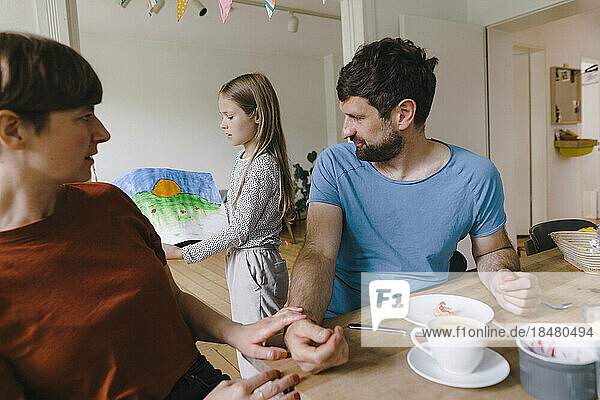 Girl showing painting to father and mother having breakfast at home