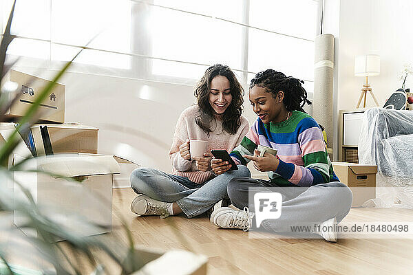 Happy young woman sharing mobile phone with friend at home