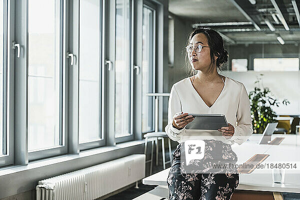 Thoughtful businesswoman holding tablet PC at office