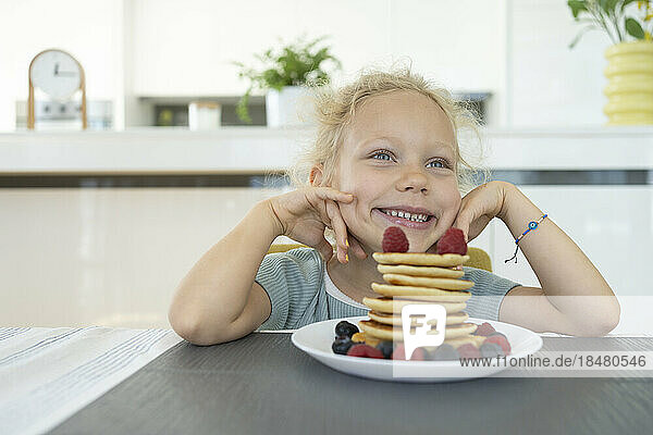 Smiling girl day dreaming by plate of fresh pancakes at home