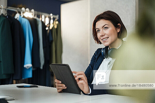 Smiling young businesswoman sitting with tablet PC at desk in office
