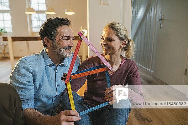 Smiling mature couple holding house model made with folding ruler at home