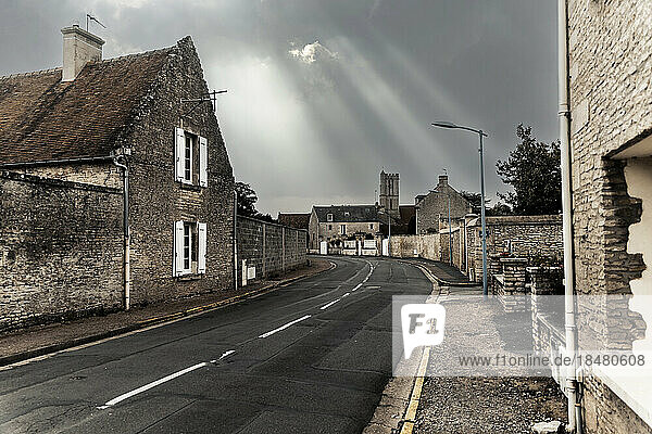 Sunlight streaming through clouds over empty street in old town
