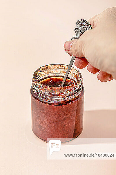 Hand of woman holding spoon with homemade strawberry jam over peach background