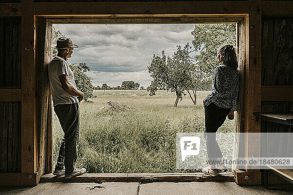 Man and woman looking at field leaning on doorway