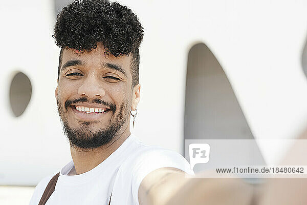 Glücklicher junger Mann  der vor dem Gebäude ein Selfie macht
