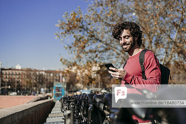 Glücklicher Mann nutzt mobile App  um an einem sonnigen Tag einen Elektroroller zu mieten