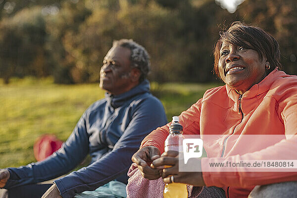 Lächelnde  nachdenkliche Frau mit Energy-Drink sitzt neben Mann im Park