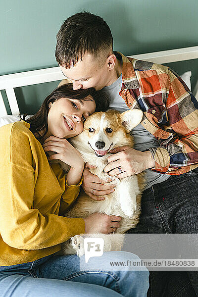 Couple embracing and playing with Pembroke Welsh Corgi sitting at home