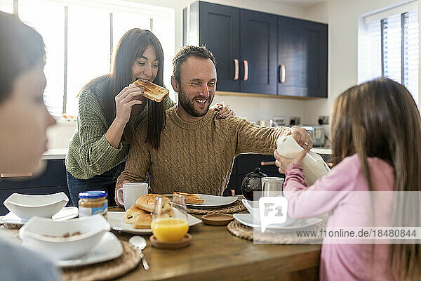 Happy man and woman having breakfast with children in kitchen