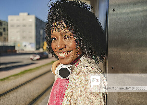 Glückliche junge Frau mit kabellosen Kopfhörern am Bahnhof