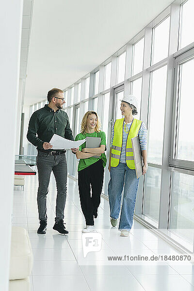 Happy businessman walking and talking with employee and engineer on office floor