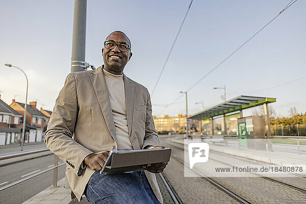Smiling mature businessman with tablet PC by tramway